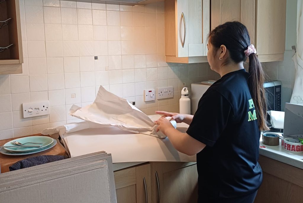 Young adult female smiling while handling a cardboard box indoors, preparing for moving day. plymouth movers