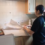 Young adult female smiling while handling a cardboard box indoors, preparing for moving day. plymouth movers
